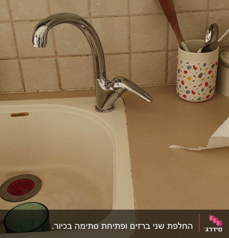 ברז מטבח כסוף מעל כיור לבן עם כוס ירוקה